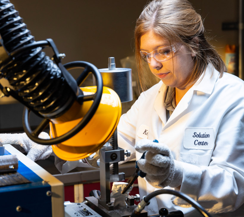 person wearing lab coat and goggles using machinery