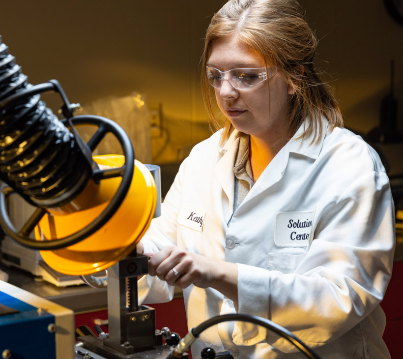 person wearing lab coat and goggles working with machine