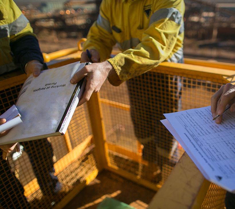 People wearing safety gear at a worksite handing each other papers.